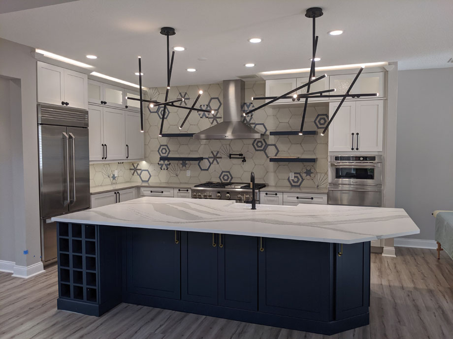 after shot of "Thomas Kitchen" with white walls, dark blue counters, and white marbled countertops. New stainless steel appliances, and geometric light fixture.